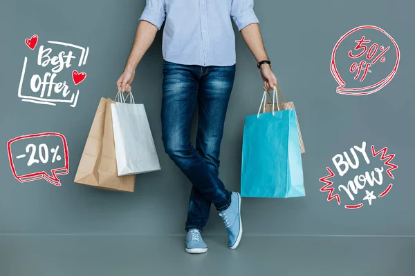 Young man holding paper bags after buying clothes on the sale