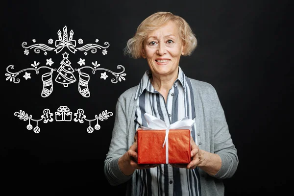 Smiling woman celebrating Christmas and holding a bright present — Stock Photo, Image