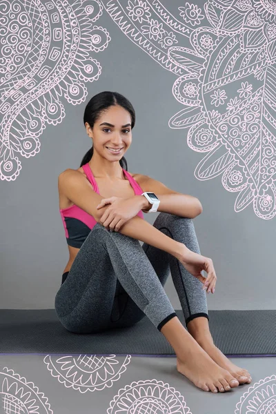 Cute sports trainer smiling and sitting on a yoga mat