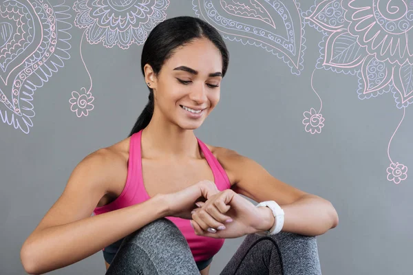 Joven alegre sonriendo mientras mira su reloj conveniente — Foto de Stock