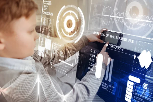 Niño serio sosteniendo un teléfono inteligente y comparándolo con su computadora — Foto de Stock