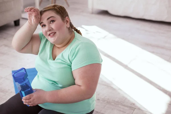 Толстая молодая женщина отдыхает после тренировки на коврике для йоги — стоковое фото