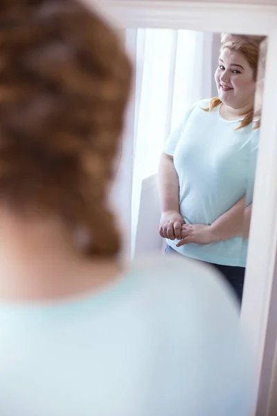 ミラーの隣に立って快適な恥ずかしがり屋の女性 — ストック写真