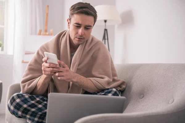 Trauriger junger Mann hält sein Smartphone — Stockfoto