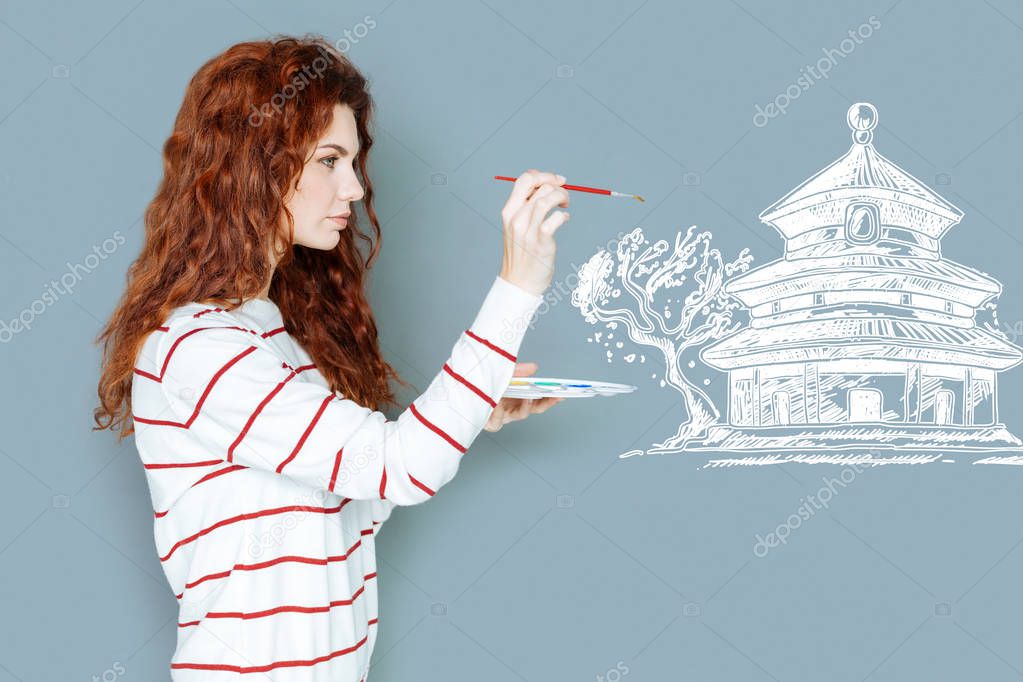 Attentive artist holding a brush and painting a house