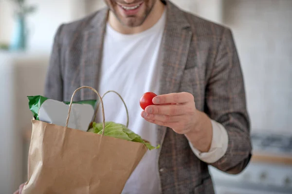 Чоловік посміхається, тримаючи маленький червоний помідор в руках — стокове фото