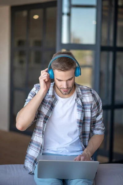 Jovem elegante ouvindo música e trabalhando no laptop — Fotografia de Stock