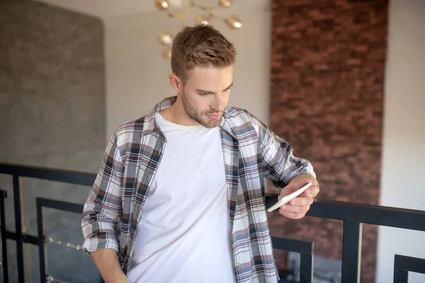 Joven hombre guapo leyendo el libro electrónico en el teléfono inteligente — Foto de Stock