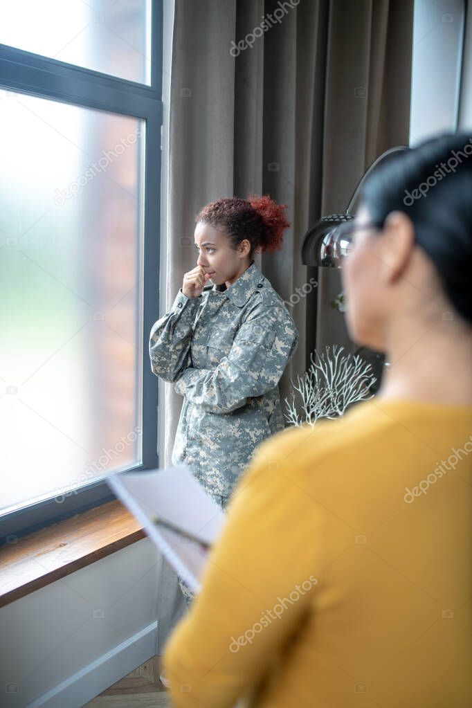 Servicewoman standing near window while visiting psychoanalyst