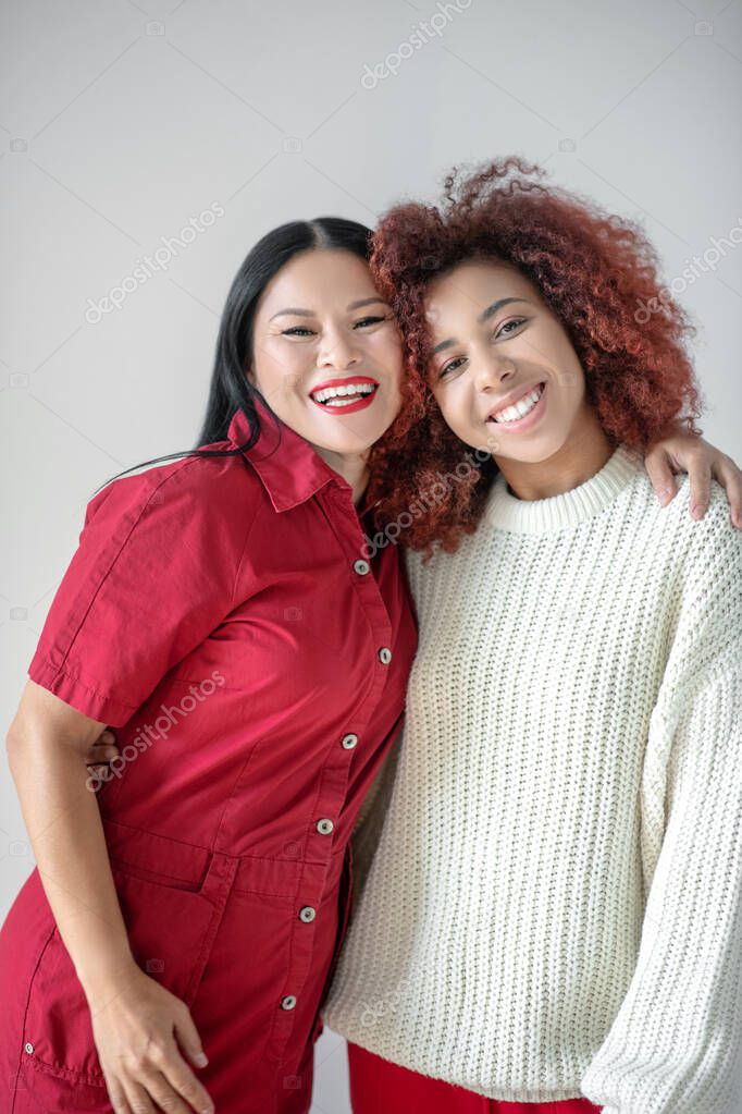 Asian beaming woman hugging her curly appealing friend