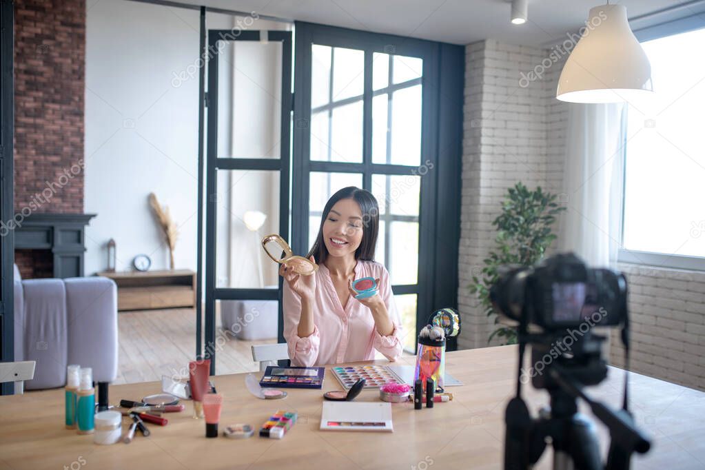 Excited beauty blogger filming video about cosmetics favorites