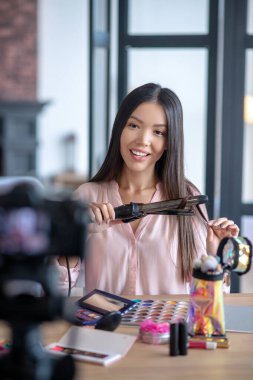 Kameranın önünde siyah gözlü bir kadın saç stili yapıyor.