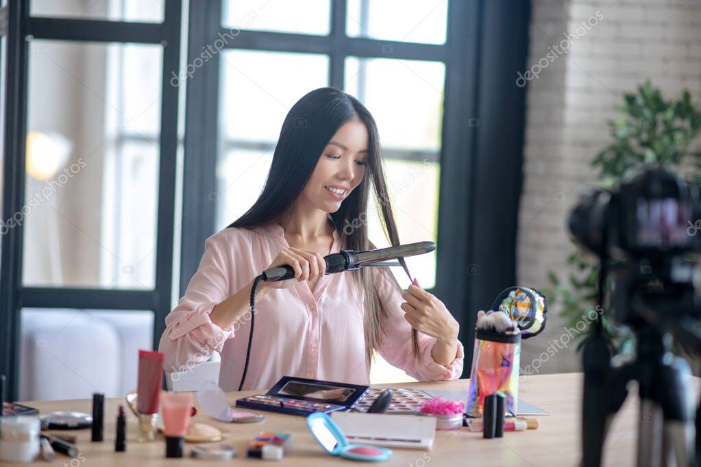 Long-haired woman curling her hair in the morning while filming blog
