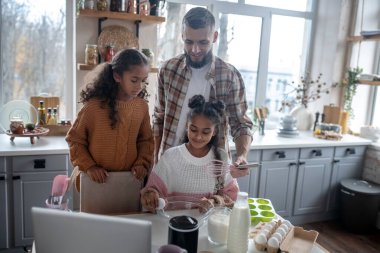 Kız kardeş ve babayla turta pişirirken yumurta kırıyor.