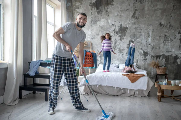 Man schoonmaken van de slaapkamer terwijl dochters plezier hebben — Stockfoto