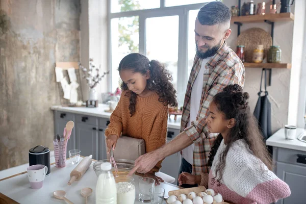 Filha tentando chicotear ovos enquanto cozinha com papai — Fotografia de Stock