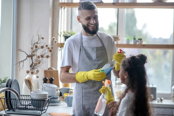 Beaming padre tomar detergentes durante la limpieza de la cocina con su hija — Foto de Stock