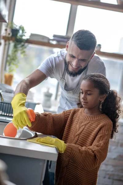 Tatínek se usmívá, zatímco roztomilá dcera čištění kuchyně — Stock fotografie