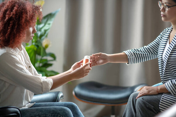 Curly red-haired woman taking sleeping pills from psychologist