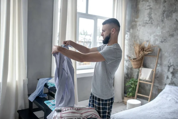 Bärtiger junger Mann im Schlafanzug bügelt Hemden — Stockfoto