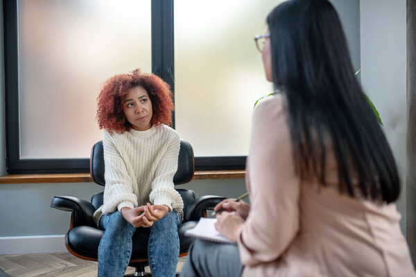 Curly woman having emotional disorder listening to psychoanalyst