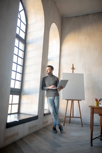 Designer standing near drawing easel holding laptop