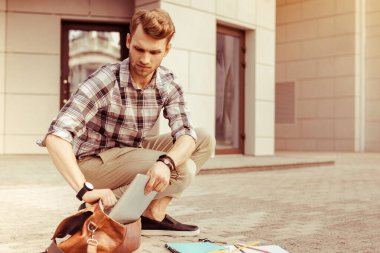 Tableti çantaya koyan ciddi sarışın adam.