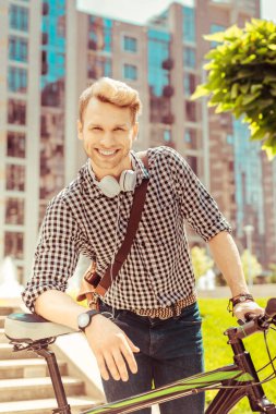 Neşeli sarışın adam bisikletine yaslanıyor.