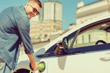 Mutlu sarışın adam elektro arabasını şarj ediyor.