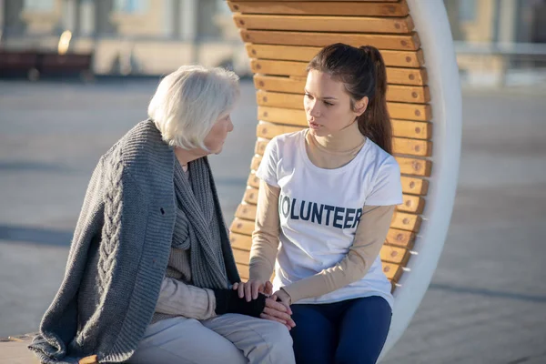 Voluntario hablando con pensionista sin hogar sentado en el banquillo — Foto de Stock