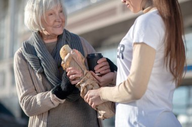 Homeless pensioner smiling while seeing volunteer with bread and tea clipart