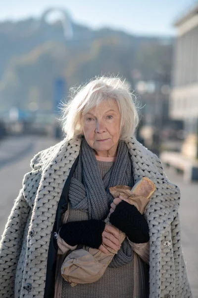 Бедная бездомная женщина в теплом пальто держит хлеб — стоковое фото