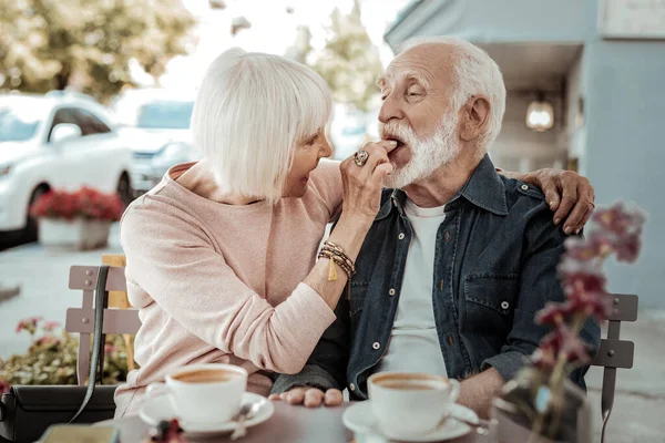 Positive nice senior woman feeding her husband