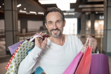 Bearded man holding many shopping bags after buying a lot of things clipart