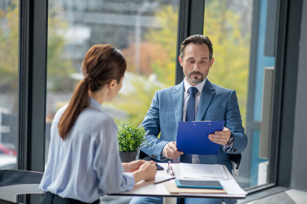 Бизнесмен читает отчет своего финансового консультанта, сидя у окна
