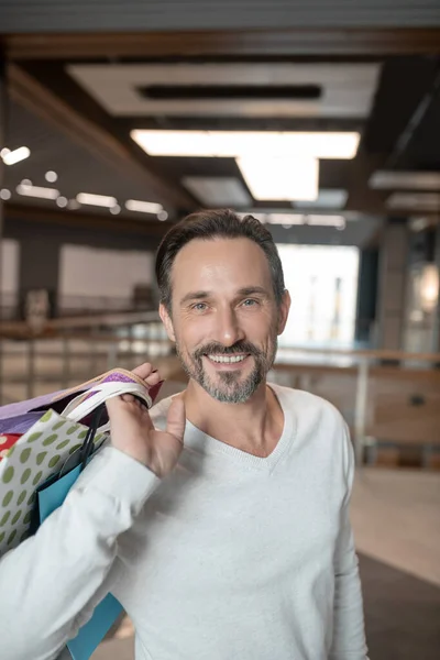 Barbudo hombre de ojos azules sonriendo mientras se siente bien después de ir de compras — Foto de Stock