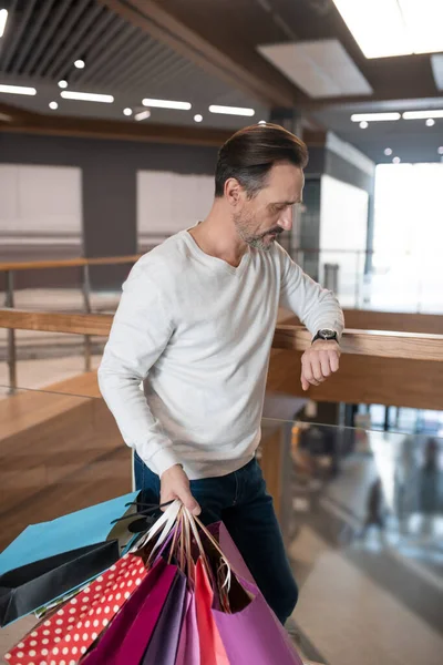 Μελαχρινός άντρας κοιτάζει το ρολόι, ενώ περιμένει τη γυναίκα του στο εμπορικό κέντρο — Φωτογραφία Αρχείου