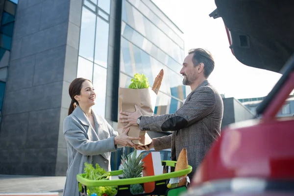 Esposa dando saco de comida para o marido, colocando tudo no carro — Fotografia de Stock