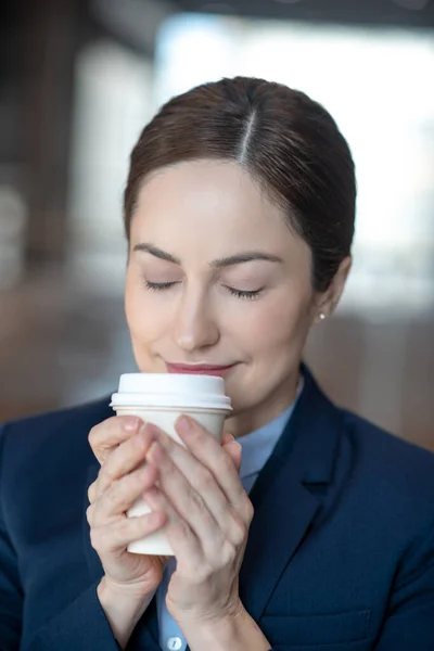 Donkerharige zakenvrouw ruikt koffie onder het genot van een drankje in de ochtend — Stockfoto