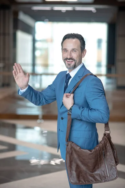 Bebaarde zakenman met bruine leren tas zwaaiende hand tijdens het verlaten van kantoor — Stockfoto