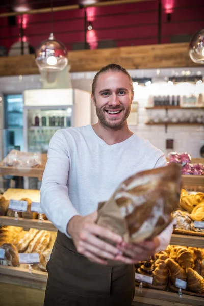 Bärtiger junger Mann lächelt, während er gerade gebackenes Brot in der Hand hält — Stockfoto
