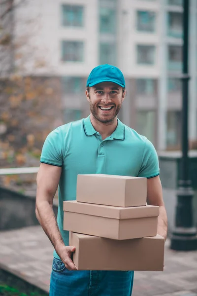Smiling delivery man wearing cap holding boxes for clients