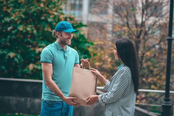 Mujer sonriendo mientras toma el bolso del repartidor hombre — Foto de Stock