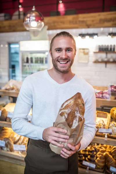 Smiling bearded man holding just baked bread standing in bakery — Stock Photo, Image