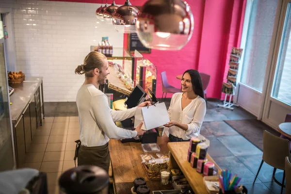 Cashier giving bag with croissants to his smiling customer — Stock Photo, Image