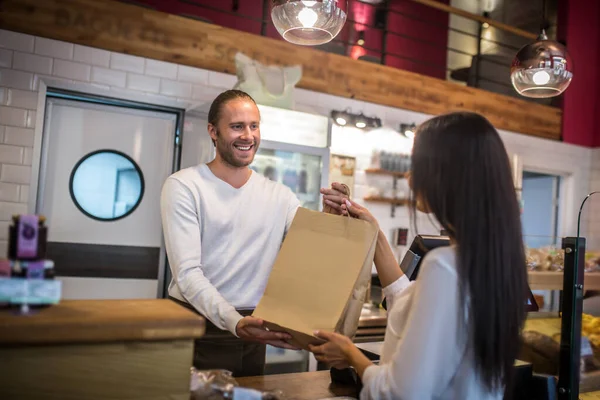Barista sonriente pasando la bolsa con café para llevar al cliente — Foto de Stock