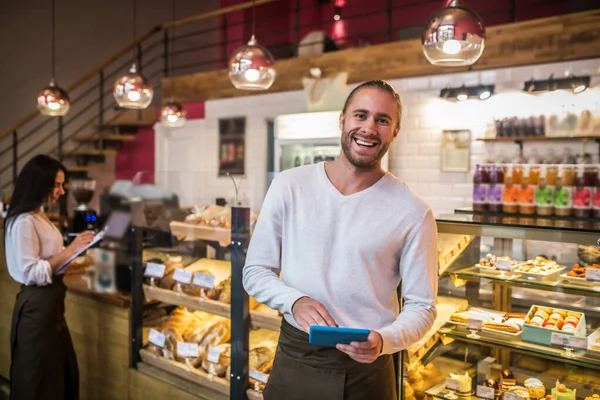 Empresario barbudo sosteniendo tableta sonriendo mientras posee panadería con esposa — Foto de Stock