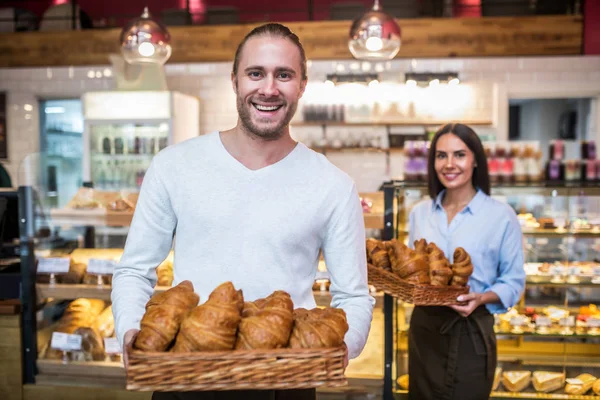 Vousatý pohledný muž se usmívá, zatímco drží croissanty v dopoledních hodinách — Stock fotografie