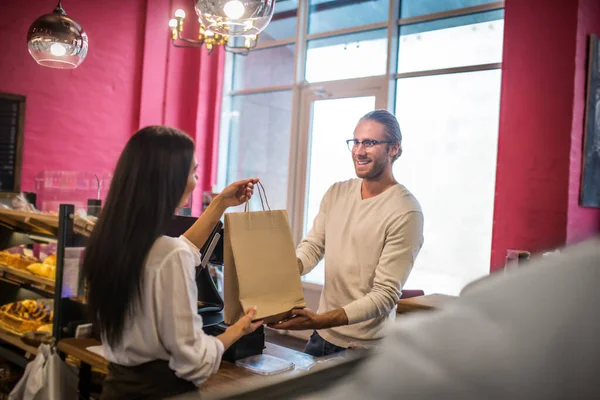 Man wearing glasses smiling while talking to cashier and buying pastry — Stock Photo, Image