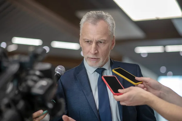 Homem de cabelos grisalhos barbudo olhando sério na conferência de imprensa — Fotografia de Stock